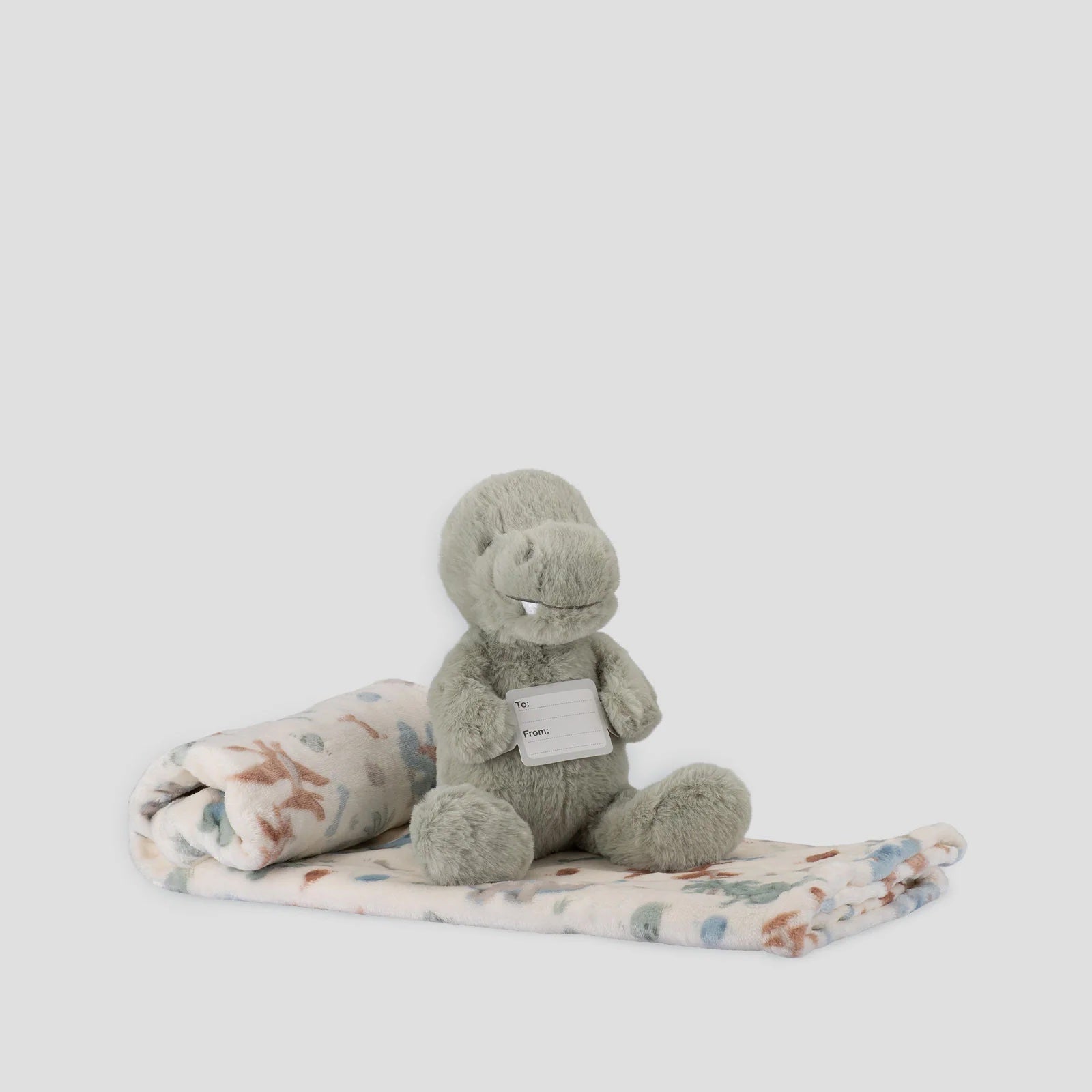 Gray plush toy with a tag on a floral blanket against a white background
