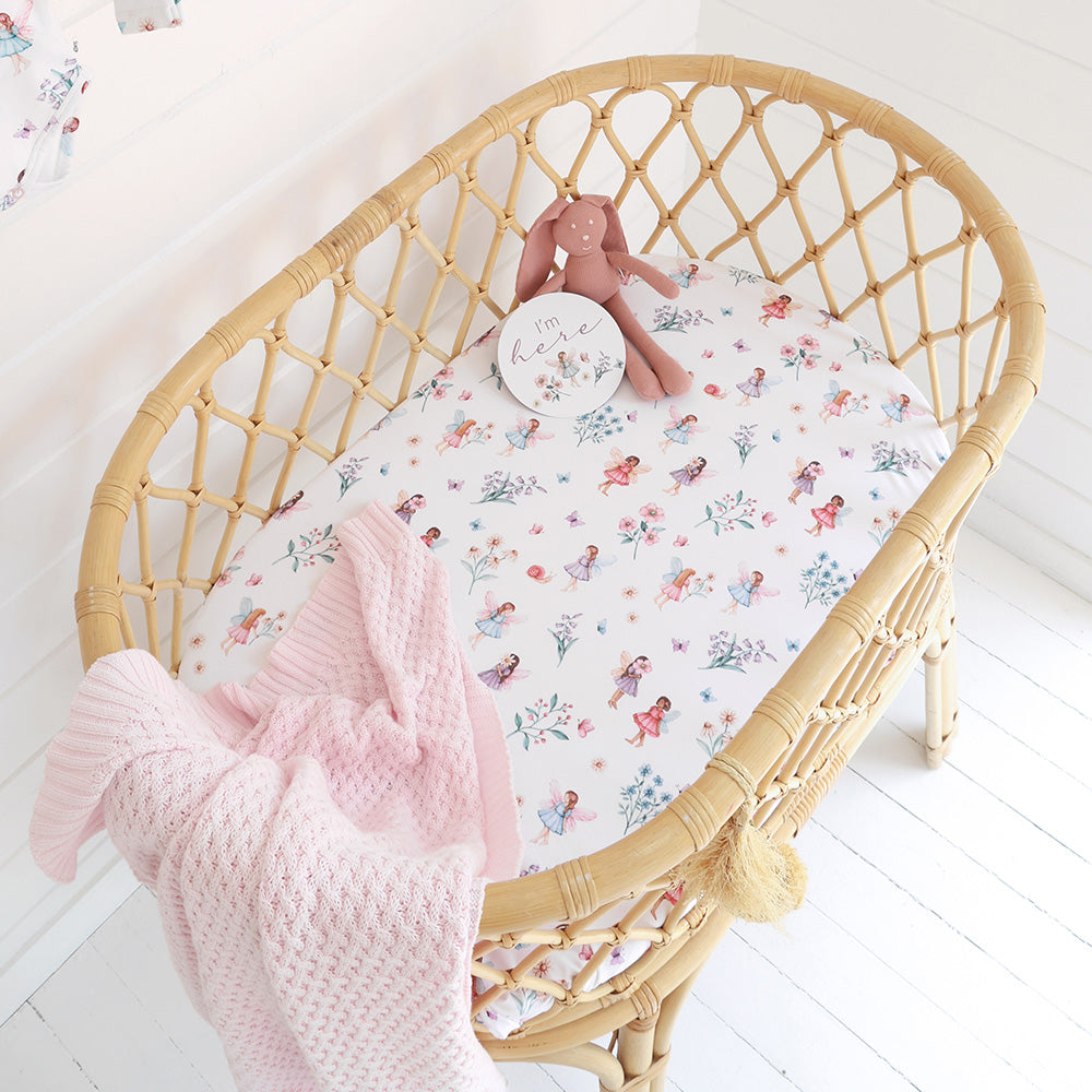 Wicker crib with floral-patterned sheet and pink blanket on a white floor
