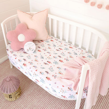 White crib with floral bedding, pink pillow, and blanket in a nursery setting.