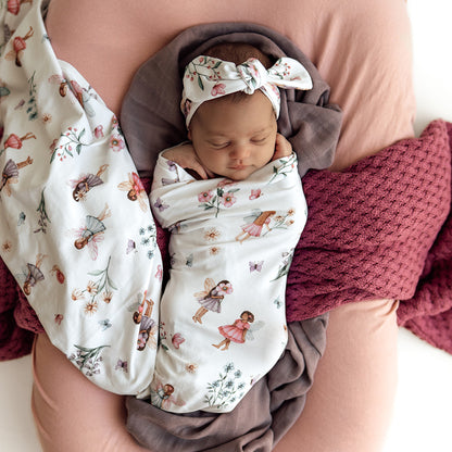 Newborn baby swaddled in a floral pattern with a headband, held by a person.
