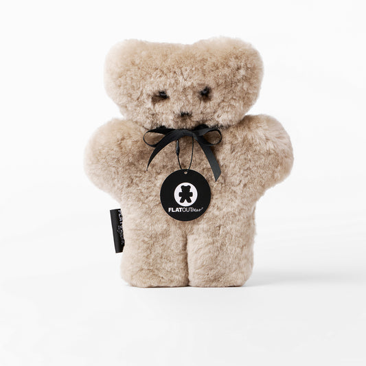 Beige teddy bear with a black tag on a white background