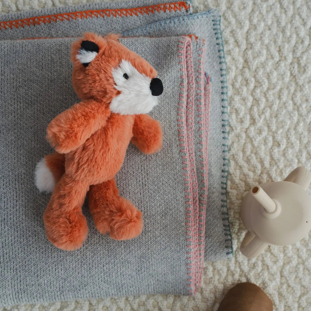 Plush fox toy on a folded blanket with brown shoes and a white toy mouse on a textured surface
