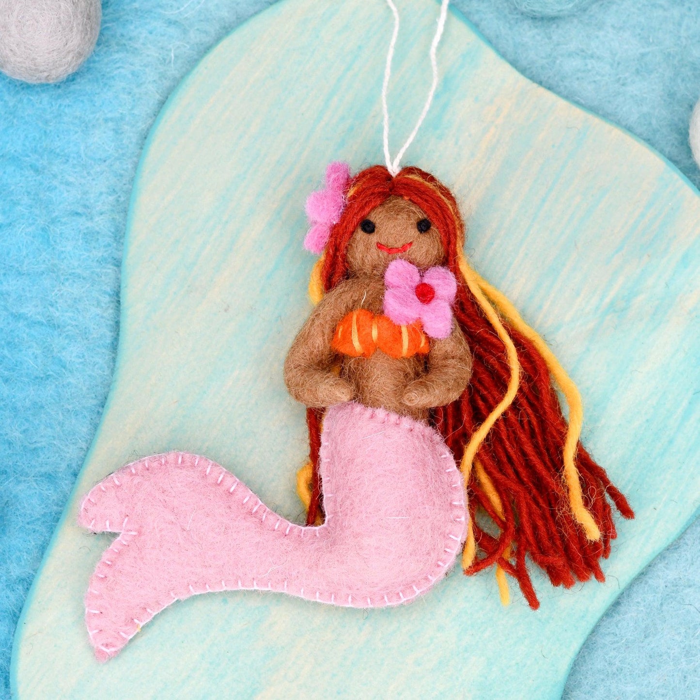 Mermaid toy with red hair and pink tail on a blue and white background
