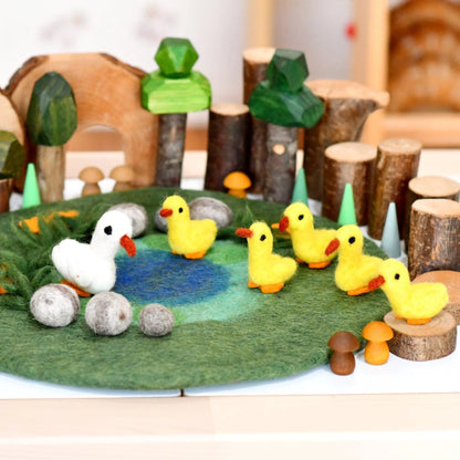 Toy ducks and a goose on a felt pond with wooden trees and logs in the background