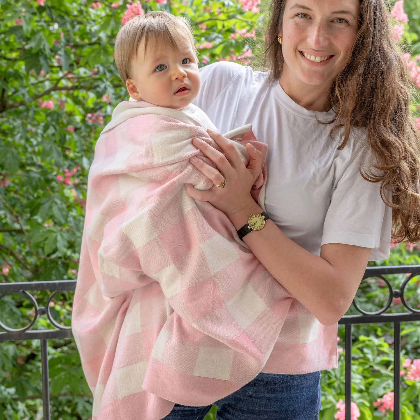 Woman holding a baby wrapped in a pink blanket with a floral background