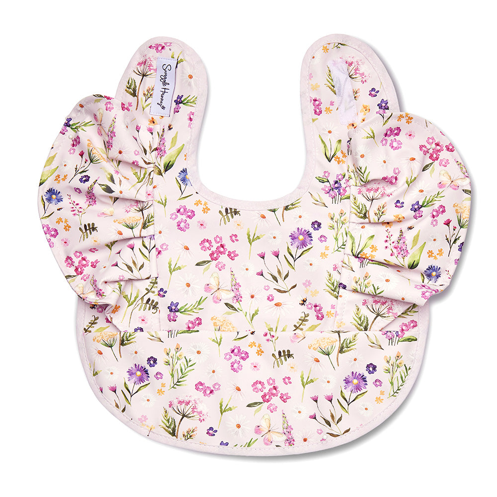 A baby bib with a ruffled neckline, featuring a delicate watercolor floral print in shades of purple, pink, and green on a pale pink background. The bib is displayed flat against a clean white background.