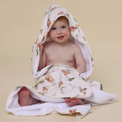 Baby wrapped in a floral-patterned hooded towel on a beige background