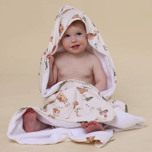Baby wrapped in a floral-patterned hooded towel on a beige background