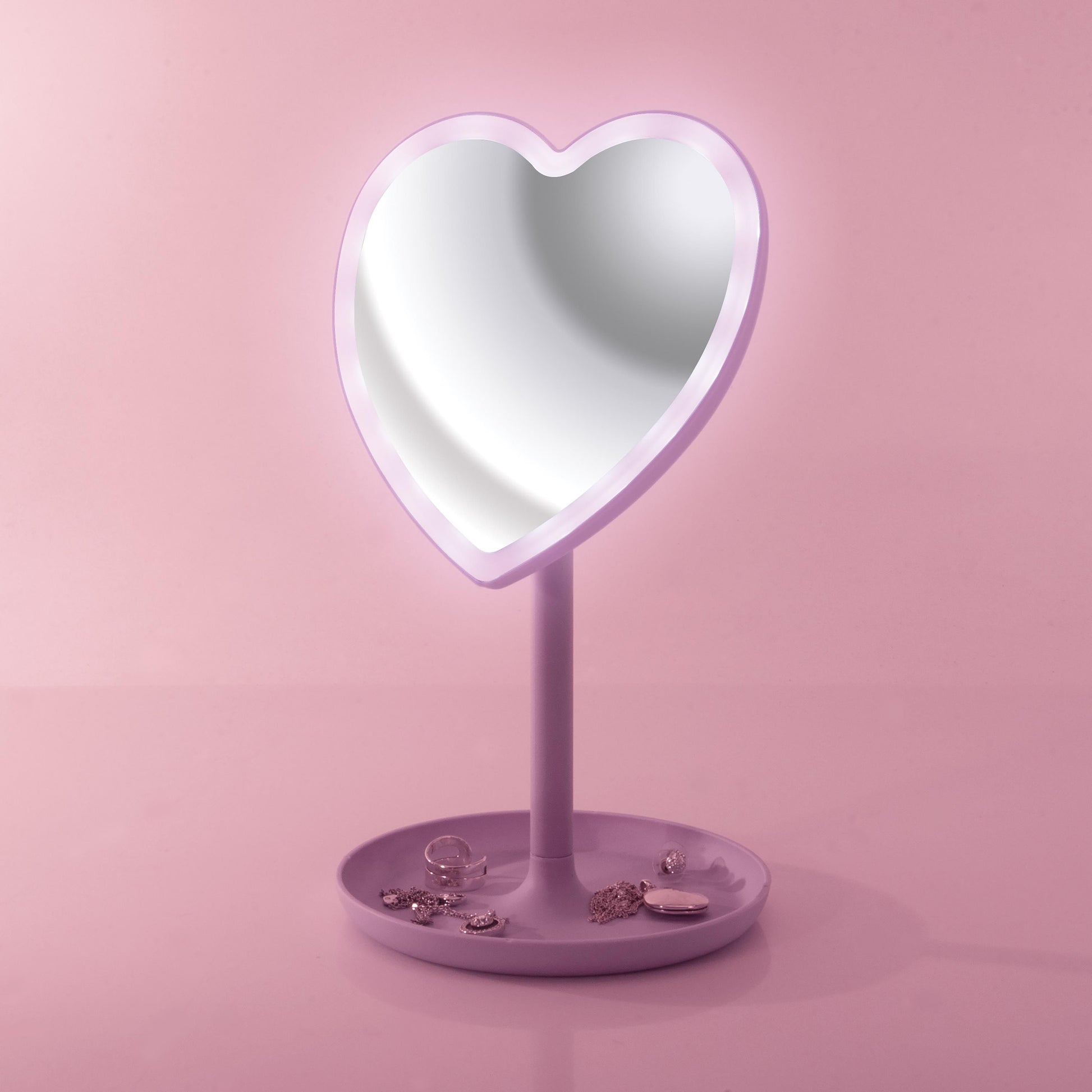Heart-shaped makeup mirror with a stand on a pink background