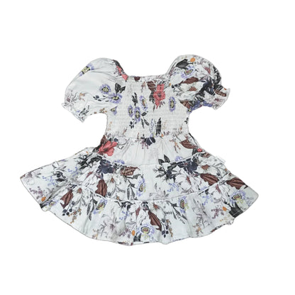 A baby girl's smocked dress with puff sleeves and a ruffled hem, featuring a white base with a colorful floral and butterfly pattern, shown on a light gray background.