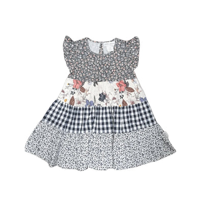 A tiered baby girl's dress with a smocked floral bodice, a central floral panel, a navy and white gingham section, and a navy and white ditsy print skirt, shown flat on a light gray background.