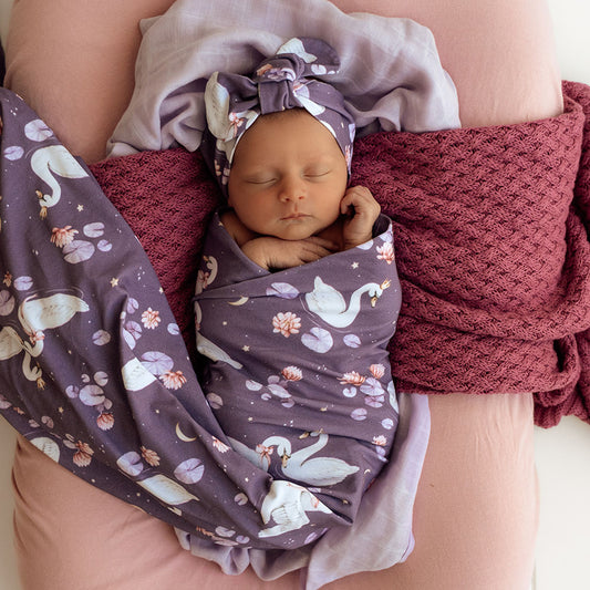 Newborn baby swaddled in a purple blanket with animal pattern, wearing a matching headband.