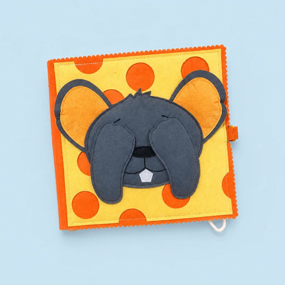 A square fabric sensory toy featuring a gray mouse face with closed eyes on a yellow background with orange polka dots, set against a light blue background.