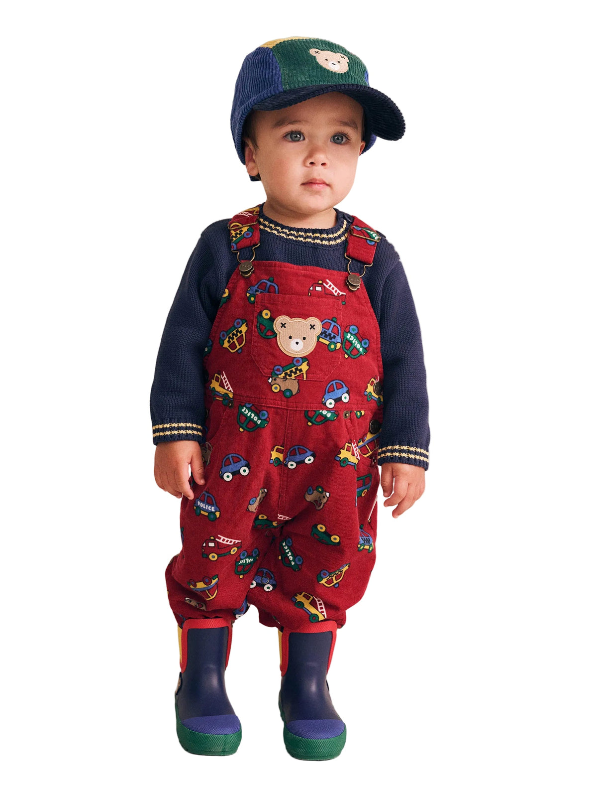 Child wearing a red patterned outfit with navy wellies and cap on a beige background