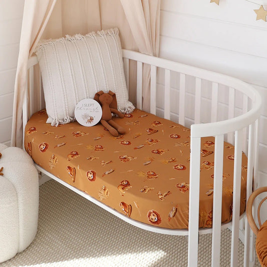 White crib with brown patterned sheet and teddy bear, surrounded by beige curtains and decor.