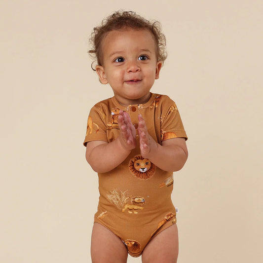 Baby wearing a brown onesie with animal prints on a beige background