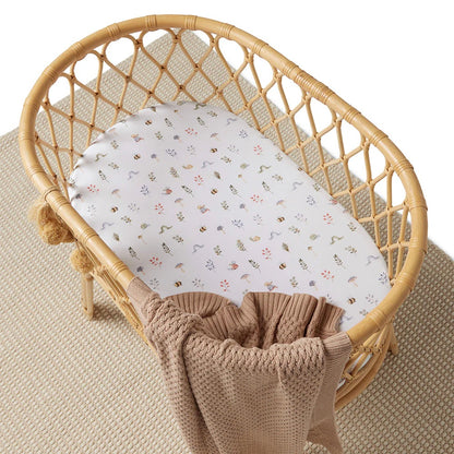 Wicker crib with a patterned sheet and brown blanket on a beige surface