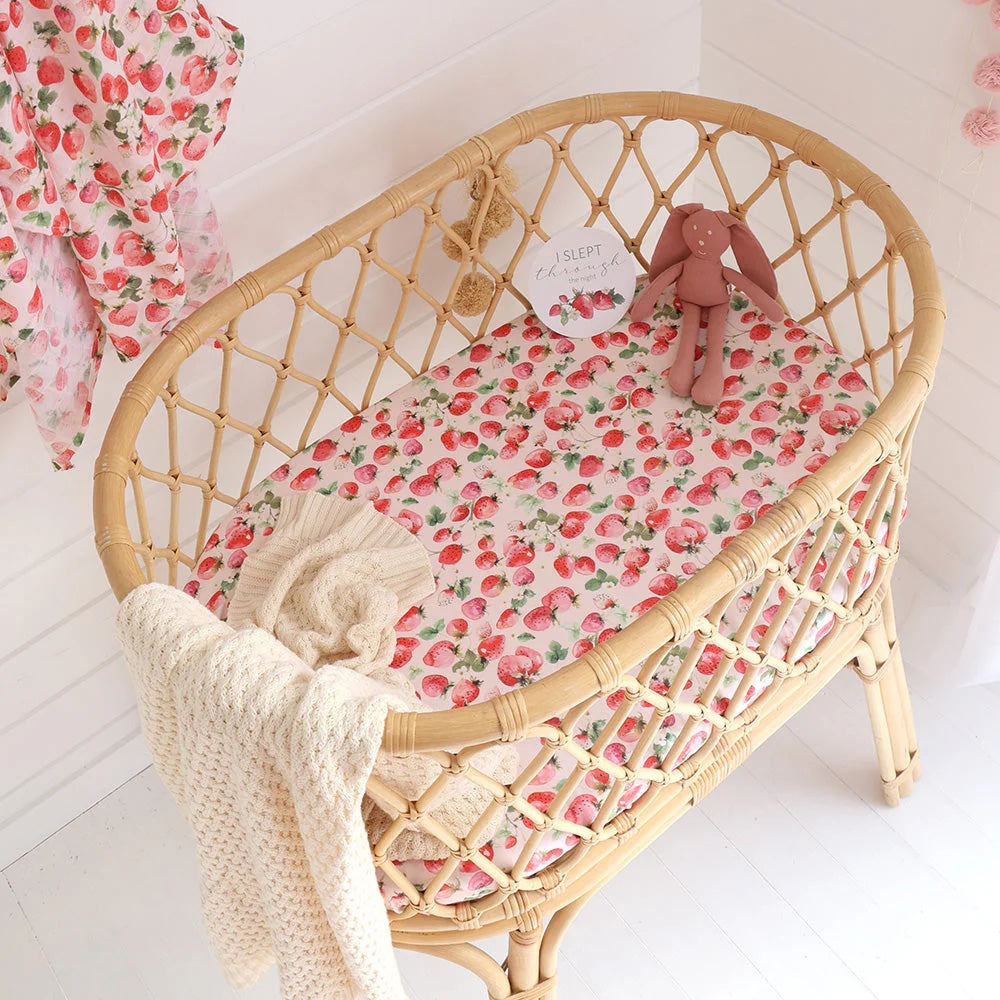 Wicker crib with floral bedding and a plush toy on a white background