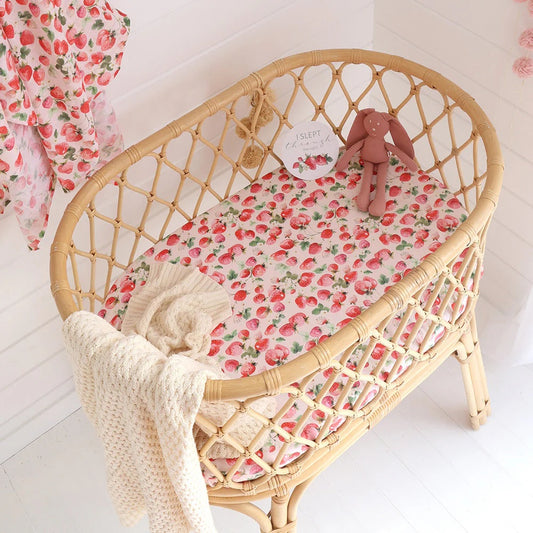 Wicker crib with floral bedding and a plush toy on a white background
