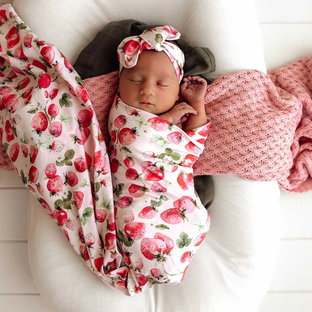 Newborn baby wrapped in a strawberry-patterned blanket with a matching headband.