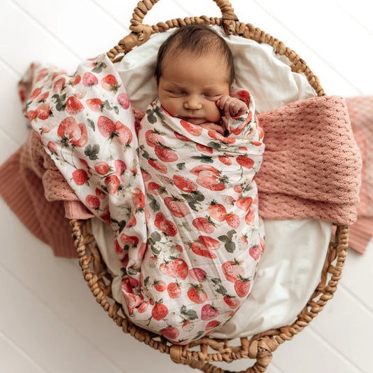 Newborn baby swaddled in a strawberry-patterned blanket in a wicker basket.