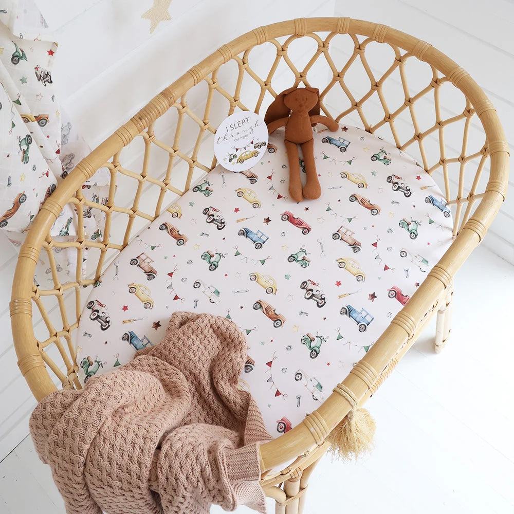 Wicker crib with patterned sheet and knitted blanket on a white floor